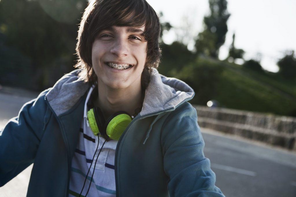 A teenage boy with headphones considering what music instrument to play since he has braces.