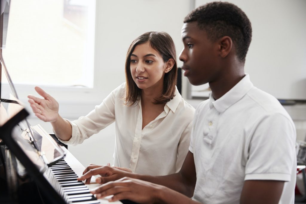 A young man studying music theory at the piano with his teacher.